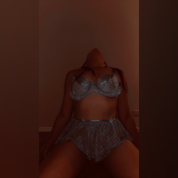 A woman sitting on the floor in a sheer lace lingerie set with a warm indoor lighting.