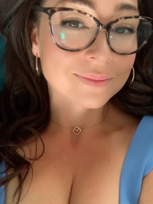 Woman with long dark hair wearing stylish glasses and a blue top, smiling at the camera.