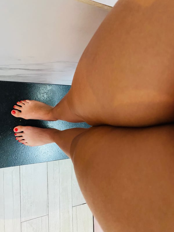 Close-up view of a person's bare feet with red nail polish standing on a dark mat in a tiled room.