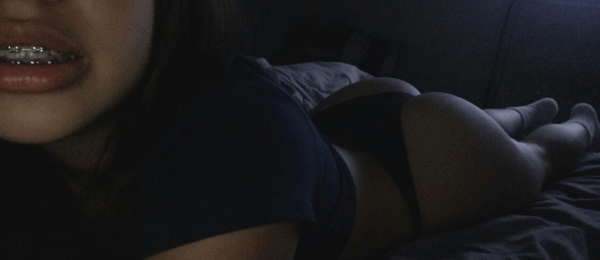 A person lying on a bed wearing a dark t-shirt and underwear, with visible braces.
