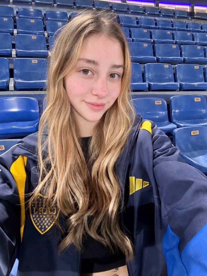 A blonde woman takes a close-up portrait indoors while seated casually.