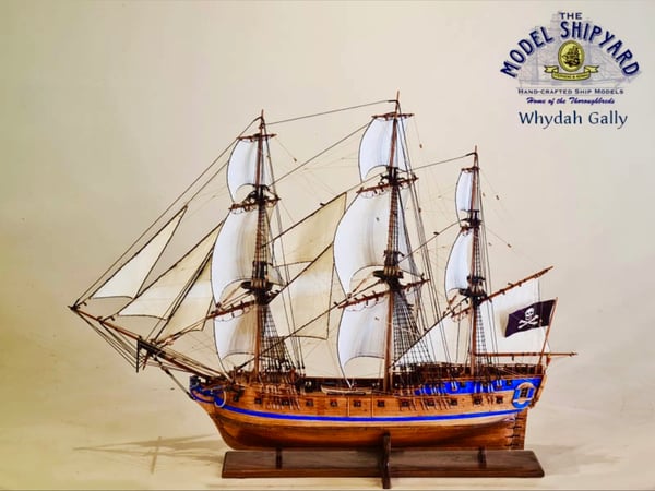 Detailed model of the Whydah Galley pirate ship with sails and Jolly Roger flag displayed on a wooden base.