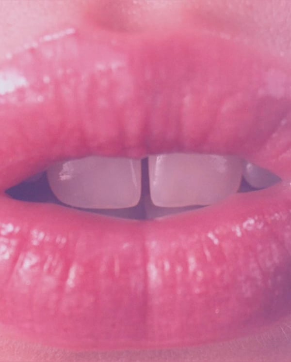 Close-up portrait of glossy pink lips with teeth slightly visible.