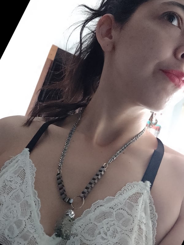 Close-up portrait of a smiling woman with long dark hair, wearing lace lingerie and layered necklaces.
