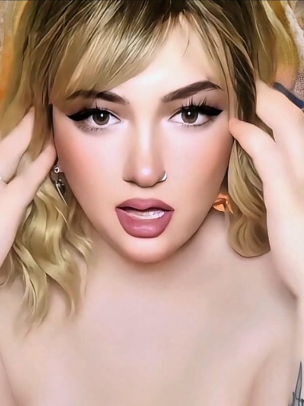 Close-up portrait of a young woman with blonde wavy hair, bold makeup, and a lip piercing, making a playful expression.