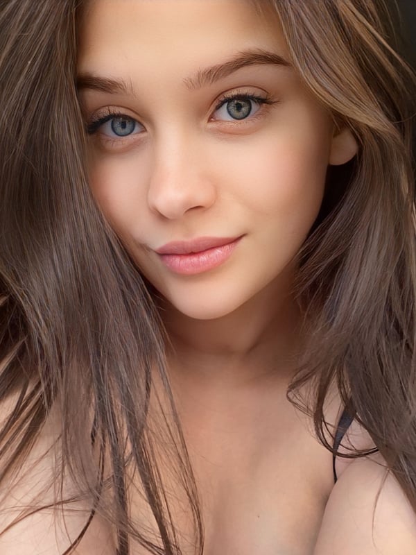 Close-up portrait of a young woman with long brown hair, blue eyes, and a subtle smile.