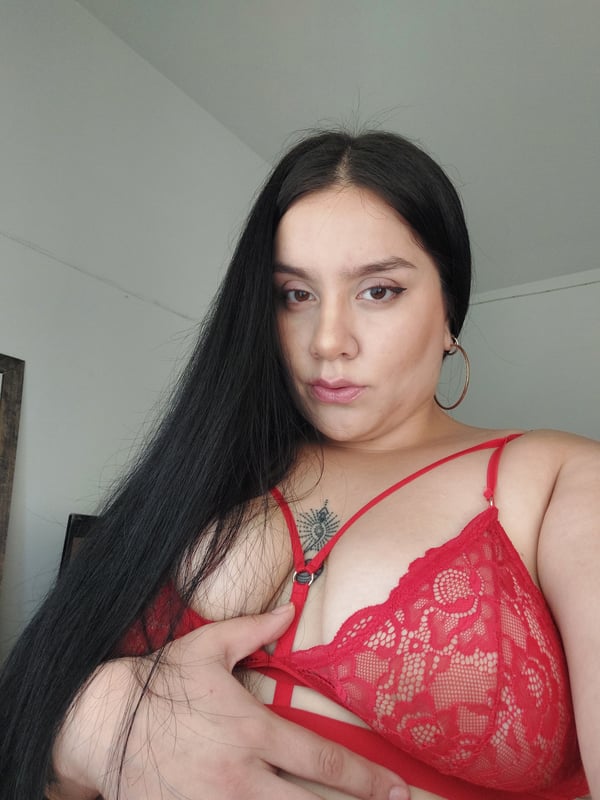 A woman with long dark hair and hoop earrings smiling at the camera while wearing a red lace top.