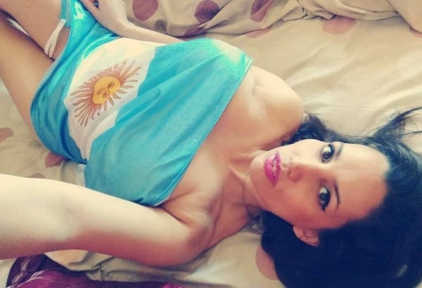 Woman reclining on a bed, draped in a blue flag with a sun emblem, posing confidently.