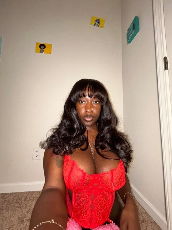 Young woman with long dark hair posing in a red lace outfit inside a room with wall art and modern decor.