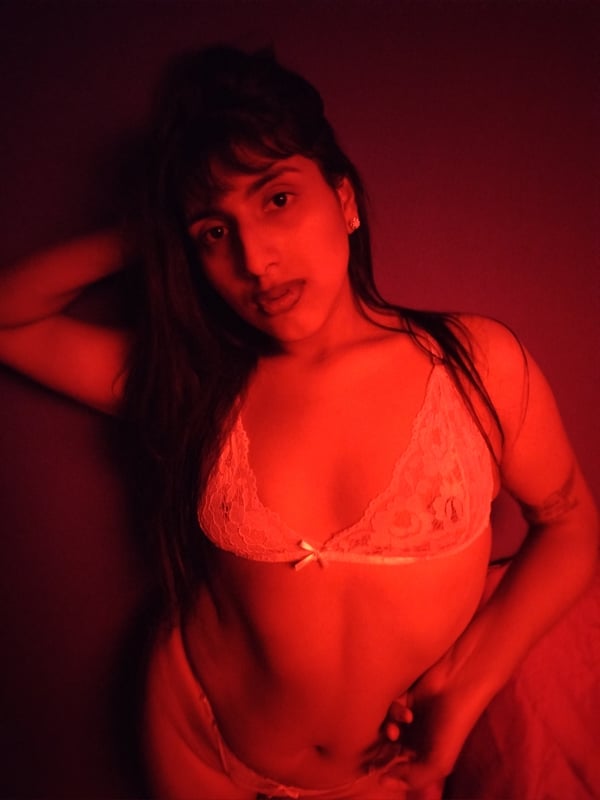 Young woman with long dark hair posing confidently in lace lingerie against a red background.