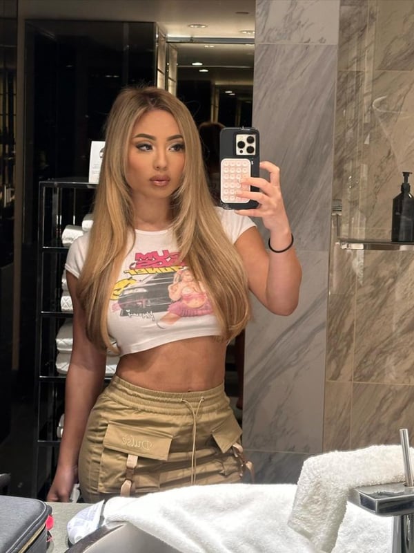 A woman taking a mirror selfie in a modern bathroom, wearing a graphic t-shirt and cargo pants.