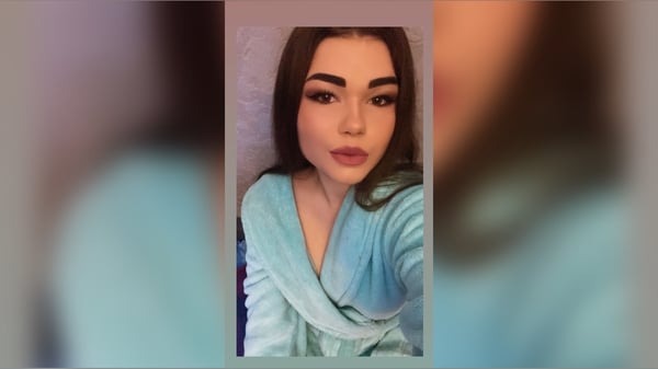 Young woman with brunette hair taking a close-up selfie in a light blue robe inside a room.