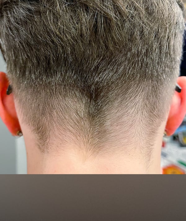 Close-up view of a person's undercut hairstyle from the back, showing long hair on top and shaved sides with visible earrings.