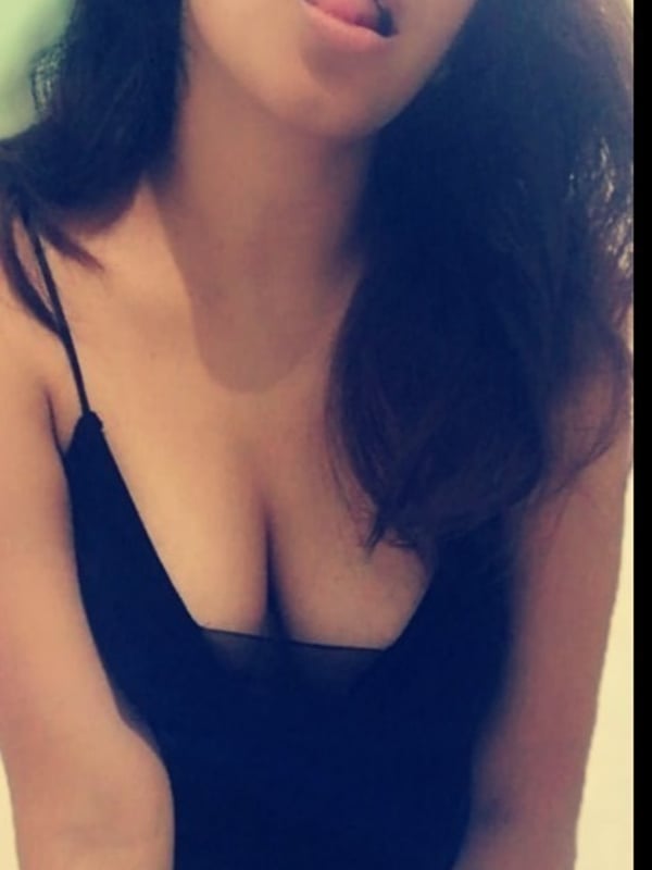A young woman with long dark hair making a playful face, wearing a black spaghetti strap top.