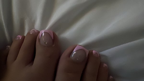 Close-up of feet with pink and white painted toenails resting on white sheets.