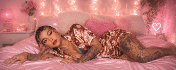 A woman posing on a pink bed with string lights and pillows in a cozy bedroom setting.
