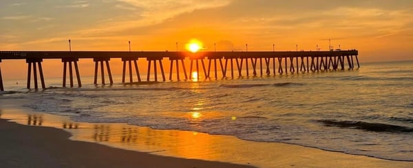 Scenic sunset view of a long pier extending over the ocean beach with waves gently lapping the shore.