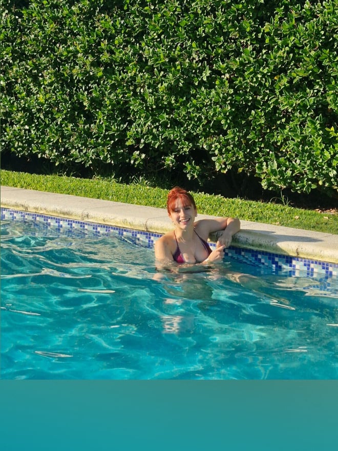 A woman with red hair relaxing in a swimming pool outdoors.