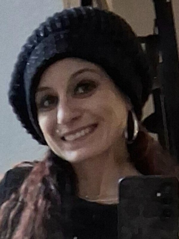 Woman smiling while wearing a knitted black hat and hoop earrings, holding a phone in front of a wooden framed mirror.