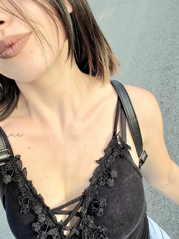 A woman with shoulder-length brown hair posing with puckered lips, wearing a black lace top with thin straps and a cross-body bag.
