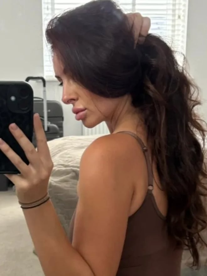 A woman with long dark hair takes a mirror selfie in a bedroom while wearing colorful attire.
