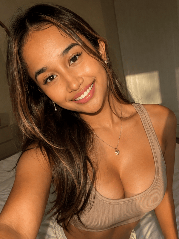 A young woman with long dark hair smiling while holding a teddy bear in a close-up selfie.