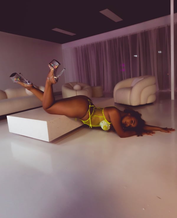 A woman posing on the floor in a bright outfit with high heels in a modern living room with white furniture and sheer curtains.
