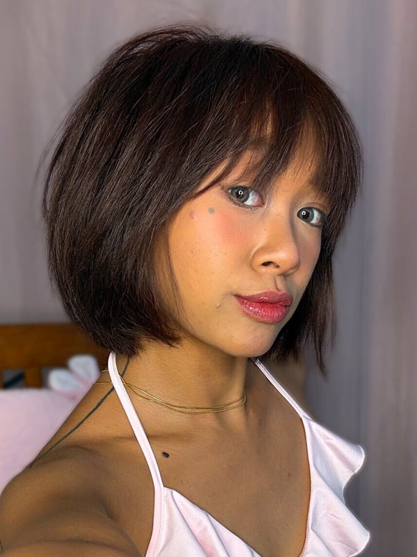 A young woman with shoulder-length dark hair smiling at the camera, wearing a light pink off-shoulder top, against a neutral background.