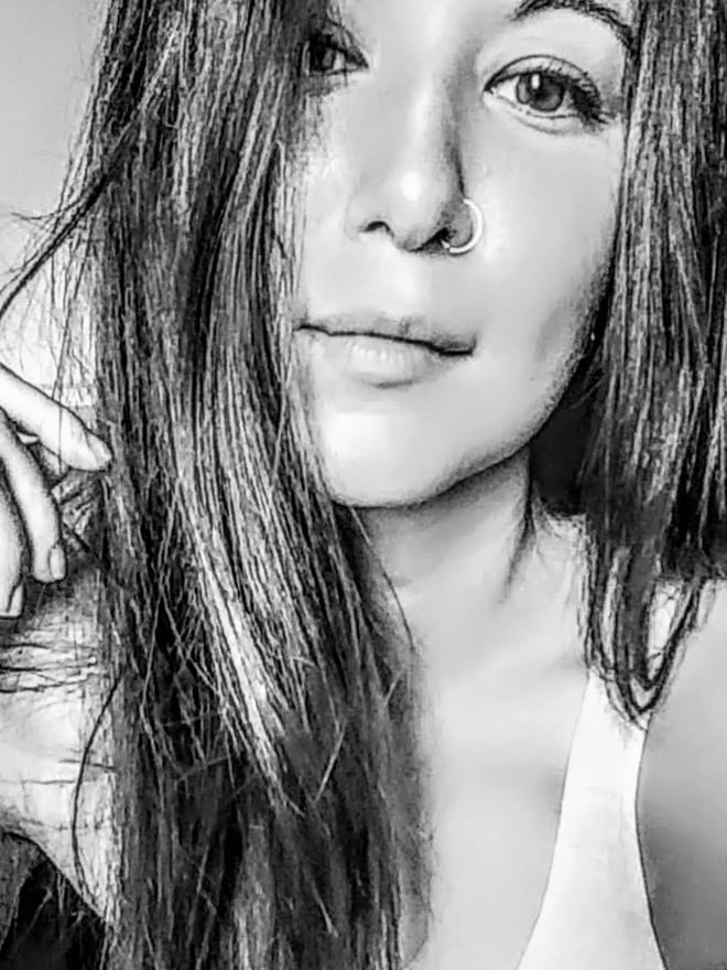 Close-up portrait of a woman with long dark hair, nose piercing, and subtle smile in black and white.