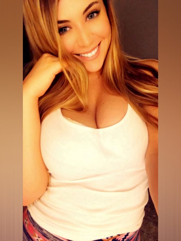 Young woman with blonde hair smiling at the camera, wearing a white tank top and colorful shorts.