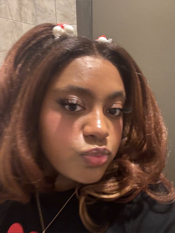 Young woman with curly brown hair adorned with white bunny ear hair clips, posing with a playful pout in front of a tiled wall.