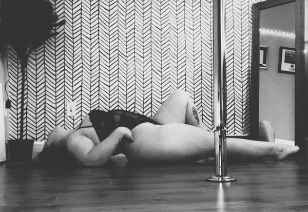 A person lying on the floor in a room with a pole and decorative wall against a neutral background.