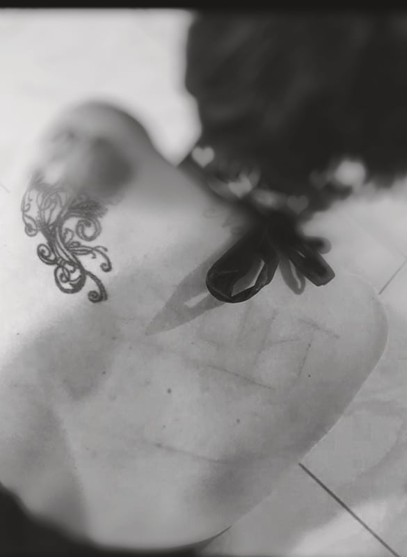 Black and white artistic photo of a woman's upper back and shoulder displaying an intricate tattoo design.