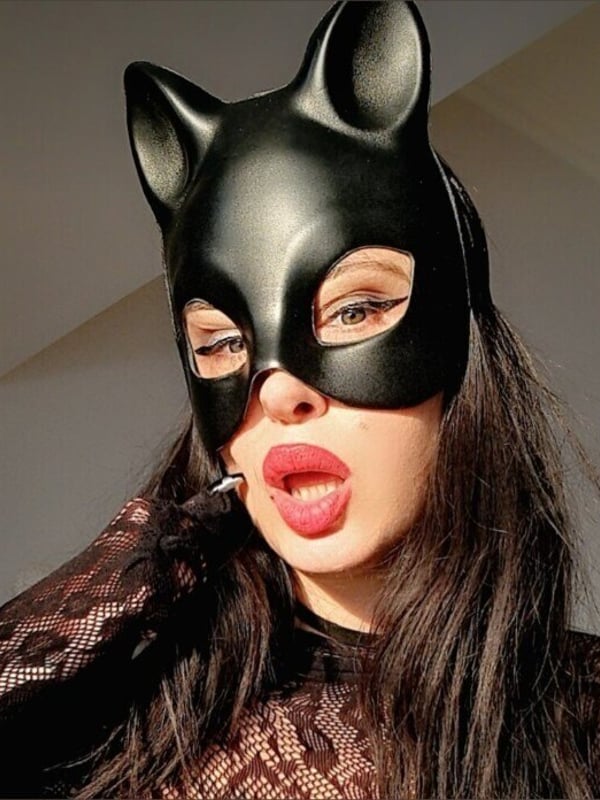 Close-up of a woman wearing a black cat mask and lace top, with glossy lips.