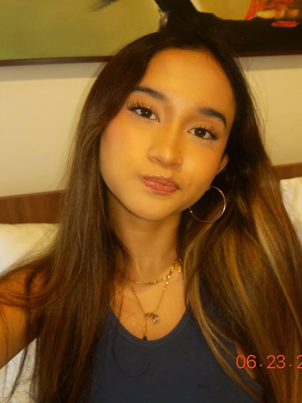 A young woman with long dark hair smiling while holding a teddy bear in a close-up selfie.