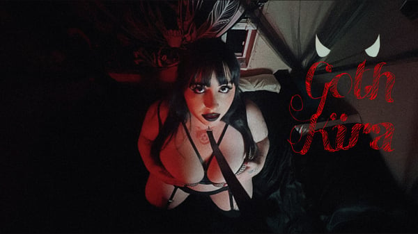 A woman with dark hair posing in gothic attire with dramatic lighting and spider web elements in a dimly lit setting.