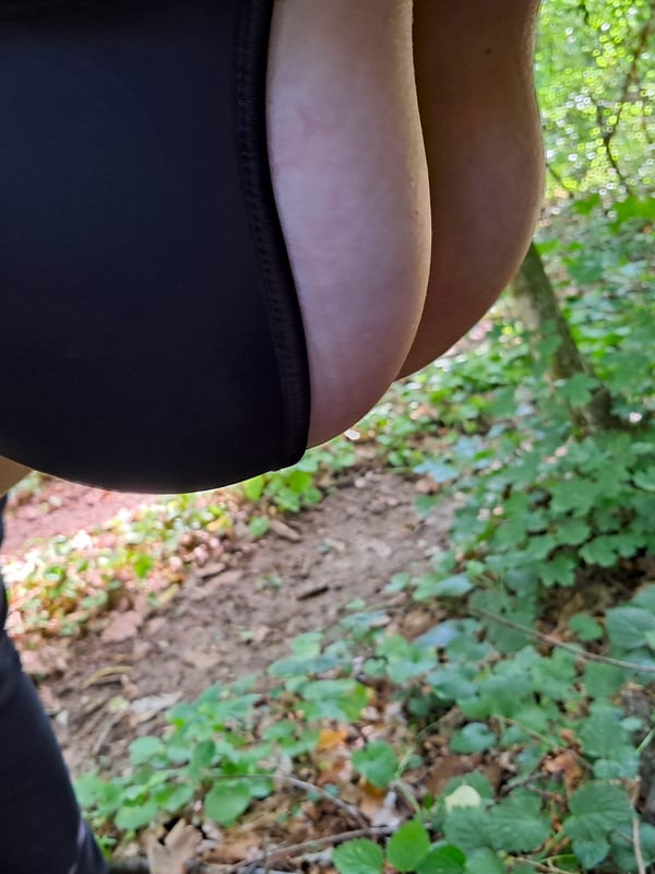 Person in black outfit and stockings posing outdoors in a lush green forest setting.