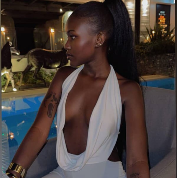 A woman with long dark hair in a ponytail poses sideways in a white halter top and pants by a lit poolside at night.