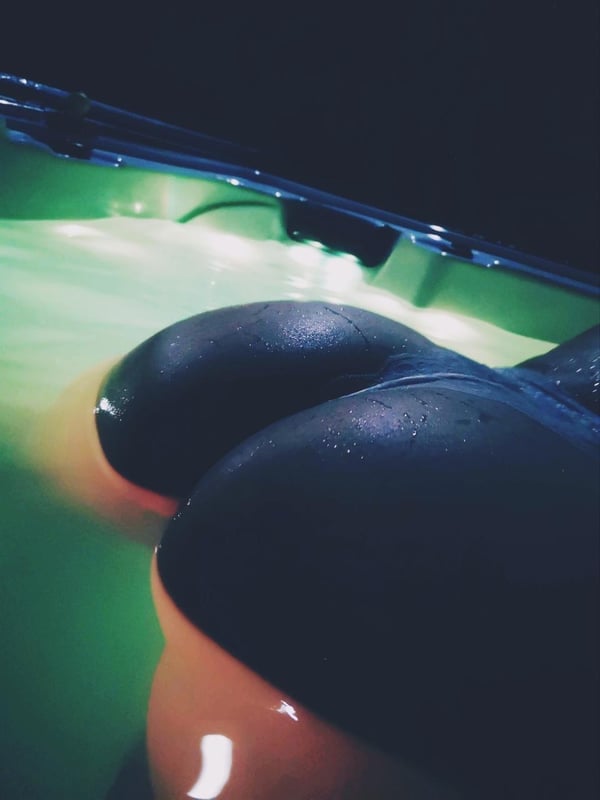 A close-up view of a woman's curvaceous figure emerging from glowing green pool water at night.