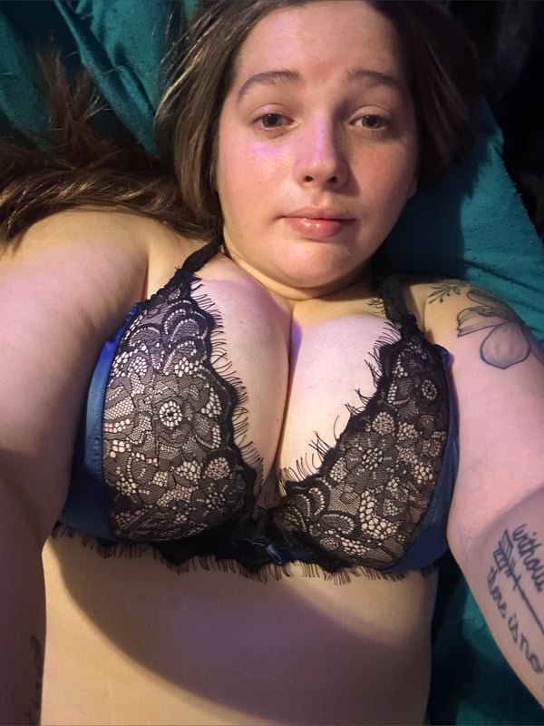 A woman lying on a bed, smiling at the camera while wearing lace lingerie in a bedroom.