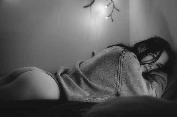 A young woman lying on a bed in a cozy room with soft lighting from decorative lights, wearing a sweater.