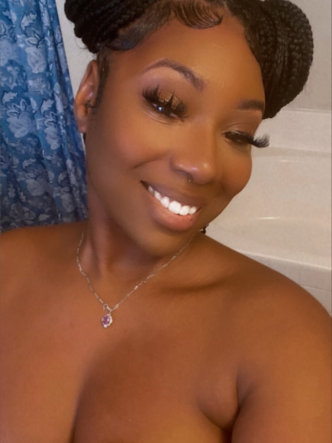 A woman with braided hair smiling in a bathroom with a blue shower curtain.