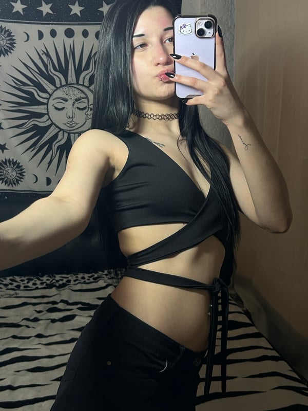 A person with dark hair taking a selfie in a bedroom setting.