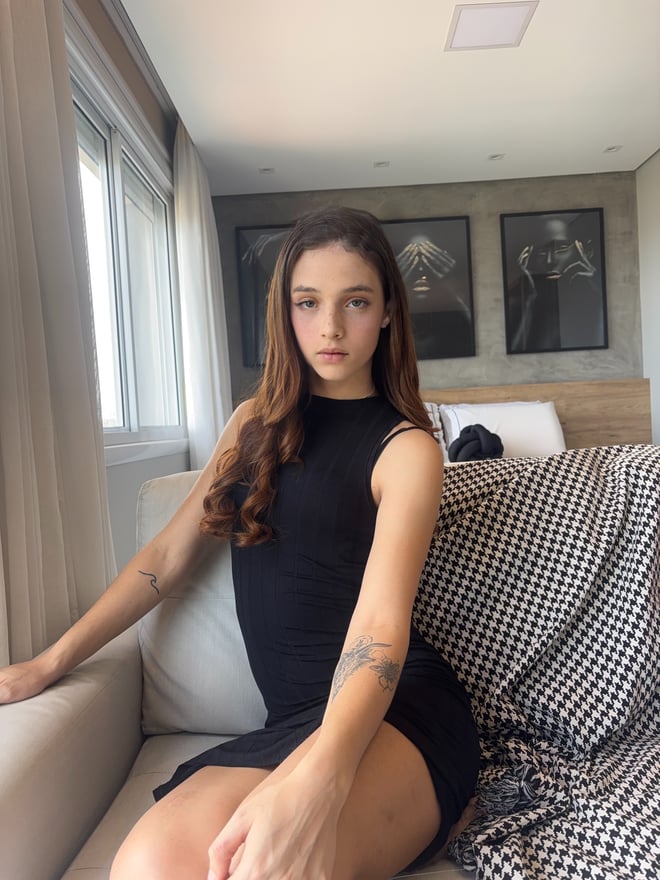 A young woman sitting on a couch in a contemporary living room with large windows and decorative elements.