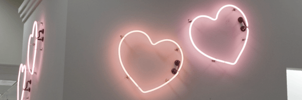 Pink neon heart lights glowing against a white wall in an indoor setting.