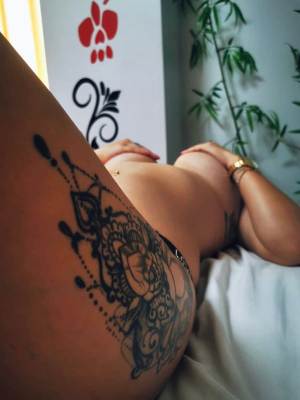 A woman reclining on a bed in a room with decorative wall art and plants, wearing lace lingerie.