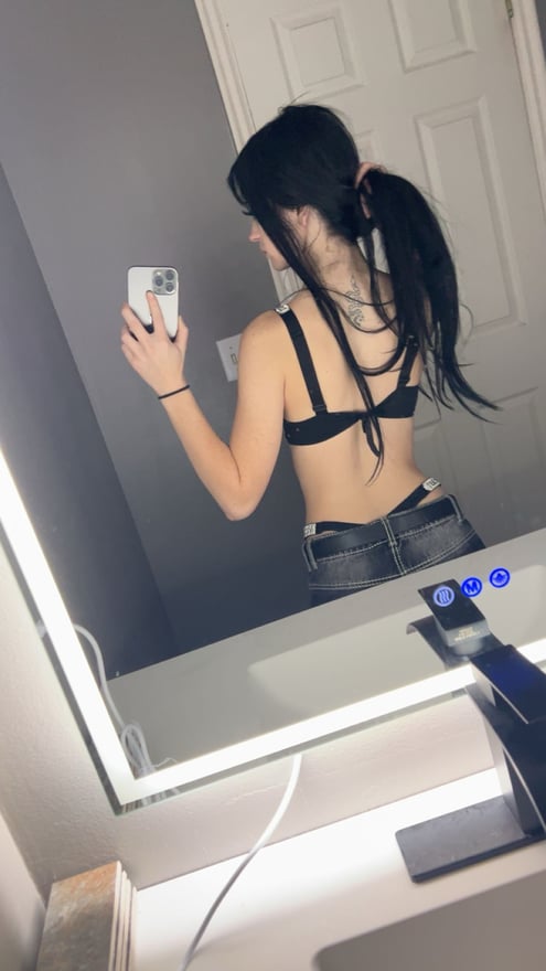 A young woman with long blue hair taking a mirror selfie indoors.