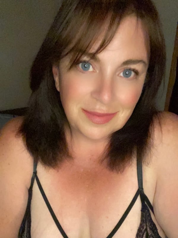 Close-up portrait of a smiling woman with brunette hair and blue eyes wearing black lace lingerie.