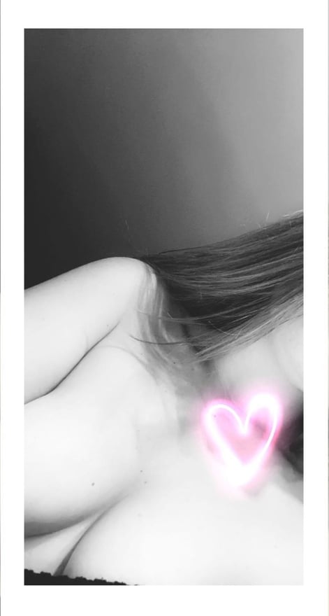 A woman with long hair lying on her side in a dimly lit setting, with a glowing pink heart effect near her chest.
