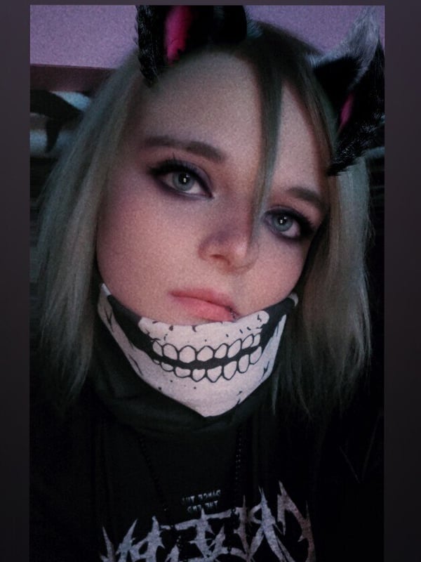 Close-up portrait of a person in gothic makeup with cat ears and a skull face covering, wearing a dark band shirt.